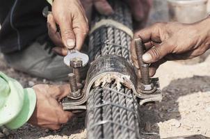 uomo del lavoro che lavora con il bullone del tendine dell'imbracatura del ponte che serra il lavoro di costruzione - la gente al concetto di lavoro di costruzione del sito foto