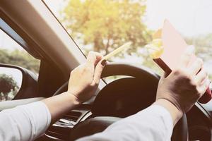 signora che mangia le patatine fritte bianche che guida l'auto pericolosamente foto