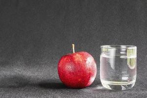 mela fresca con un bicchiere di acqua potabile pulita su sfondo grigio - concetto di sfondo pulito frutta fresca e acqua foto