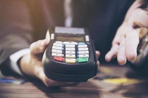 la mano dell'uomo del commerciante usando la macchina della carta di credito foto