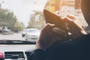 l'uomo guarda il suo portafoglio vuoto mentre guida l'auto, comportamento pericoloso foto