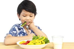 Asian bel ragazzo mostrando godere di espressione con verdure fresche colorate e bicchiere di latte isolato su sfondo bianco foto