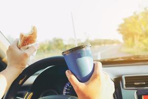 l'uomo sta mangiando pericolosamente hot dog e bevande fredde mentre guida un'auto foto