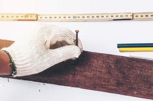 foto d'epoca della mano che tiene il chiodo pronto per metterlo nella barra di legno sopra altri strumenti su sfondo bianco