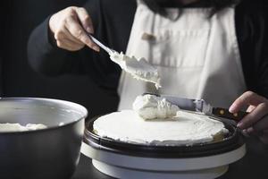 signora che fa la torta mettendo la crema con la spatola - concetto di cucina da forno fatto in casa foto