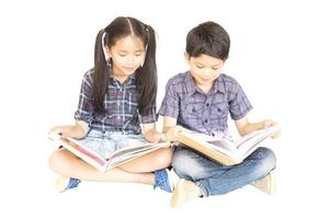10 e 7 anni ragazza e ragazzo asiatici della scuola che si siedono felicemente e che leggono insieme il libro isolato sopra bianco foto