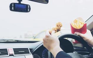 uomo d'affari che guida l'auto mentre mangia pericolosamente pollo fritto e patatine fritte foto