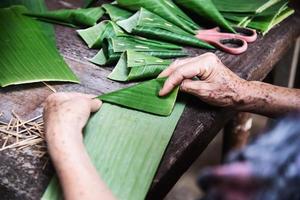 le mani della vecchia nonna che lavorano con la foglia di banana per la realizzazione di contenitori di fiori - persone che realizzano oggetti tradizionali per la partecipazione alla cerimonia locale foto
