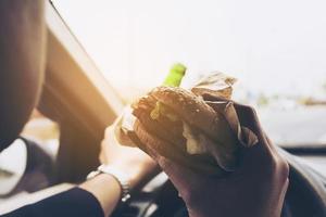 uomo che guida l'auto mentre mangia hamburger e beve birra foto