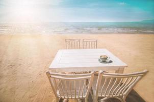 set bianco di sedie rilassanti e tavolo con una tazza di caffè sulla spiaggia di pataya, in Thailandia con cielo blu e sfondo chiaro del sole foto