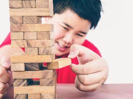 il tono vintage del bambino asiatico sta giocando al gioco della torre di blocchi di legno per praticare abilità fisiche e mentali. la foto è focalizzata sulle mani.