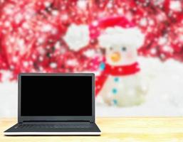 laptop su tavolo di legno bianco uomo di neve sfocato su uno sfondo bianco e decorato di rosso natale e capodanno. foto