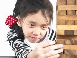 il bambino asiatico sta giocando al gioco della torre di blocchi di legno per praticare abilità fisiche e mentali. la foto è focalizzata sul viso del modello e isolata su bianco.