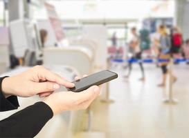 l'uomo d'affari sta usando - toccando il telefono cellulare su viaggiatori sfocati e banco del check-in nel terminal dell'aeroporto foto