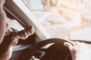 uomo che mangia ciambelle mentre guida l'auto - concetto di guida non sicuro multitasking foto