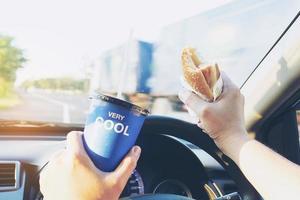 l'uomo sta mangiando pericolosamente hot dog e bevande fredde mentre guida un'auto foto