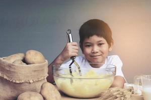 Ragazzo di 7 anni che prepara felicemente purè di patate foto