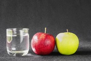 mela fresca con un bicchiere di acqua potabile pulita su sfondo grigio - concetto di sfondo pulito frutta fresca e acqua foto