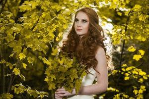 giovane donna in possesso di un mazzo di foglie d'acero gialle. ritratto autunnale di giovane donna. ragazza dai capelli rossi nella foresta d'autunno foto