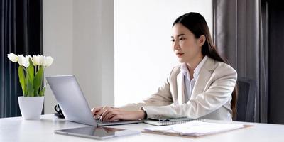 vista frontale di una bella donna d'affari asiatica che lavora su una tazza di caffè tablet posta sul tavolo dell'ufficio. foto