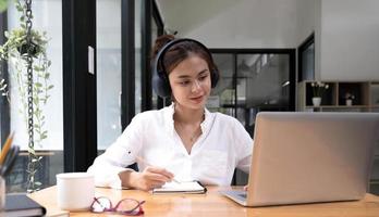 l'interprete donna asiatica scrive la traduzione dalla lingua straniera all'inglese ascolta la registrazione audio in cuffia. foto