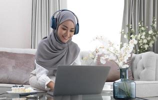 tutoraggio online. insegnante di giovane donna musulmana che fa una videochiamata con gli studenti, parla alla fotocamera del laptop, si siede sul divano a casa foto