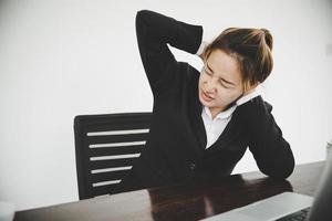 la giovane donna asiatica è seduta al lavoro e ha dolore al collo foto
