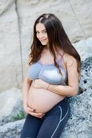 donna incinta con capelli lunghi sani e fiori. bella ragazza che aspetta il bambino. la futura mamma le abbraccia la pancia. foto