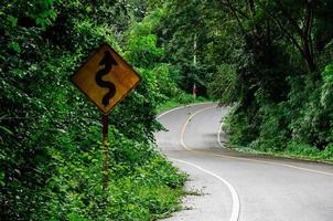 vecchio segnale stradale posto accanto lungo la strada disordinata da alberi ed erba. foto