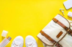 borsa per il trasporto, scarpe, telefono cellulare e auricolari con forniture su sfondo giallo per il concetto di ritorno a scuola. foto