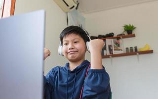 ragazzo asiatico sorridente che chiacchiera con gli amici o uno studente che studia Internet sui social network seduto davanti al laptop a casa. chattare sui social media e videoconferenza. foto