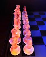 scacchi di vetro sulla scacchiera illuminata dalla luce blu e arancione foto