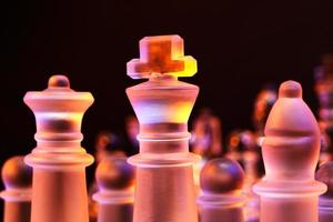 scacchi di vetro sulla scacchiera illuminata dalla luce blu e arancione foto