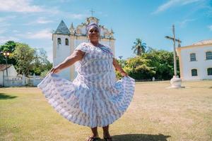 felice donna brasiliana di origine africana vestita con un tradizionale abito bahiano che balla davanti alla chiesa foto