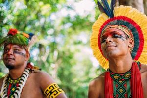 indiano della tribù pataxo. indiano brasiliano del sud di bahia con copricapo di piume, collana e tradizionali dipinti facciali che guardano a sinistra foto