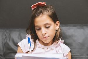 bambina che scrive nel quaderno. bella studentessa elementare che studia nel divano. foto