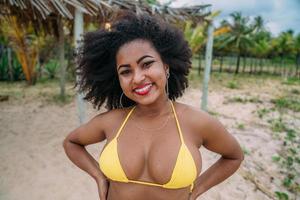 bella donna latinoamericana in bikini sulla spiaggia. giovane donna godendo le sue vacanze estive in una giornata di sole, sorridente e guardando la telecamera foto
