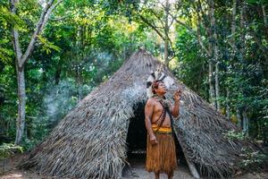 sciamano della tribù pataxo, che indossa un copricapo di piume e fuma la pipa. indiano brasiliano guardando a destra foto