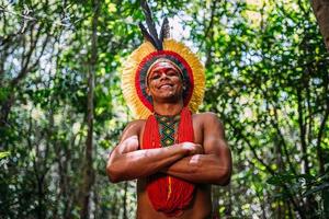 indiano della tribù pataxo, con copricapo di piume. giovane indiano brasiliano che guarda l'obbiettivo, sorridente e le braccia incrociate foto