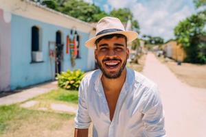 turista che fa selfie nel centro storico di porto seguro. uomo latinoamericano in cappello che sorride alla macchina fotografica foto