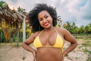 bella donna latinoamericana in bikini sulla spiaggia. giovane donna godendo le sue vacanze estive in una giornata di sole, sorridente e guardando la telecamera foto