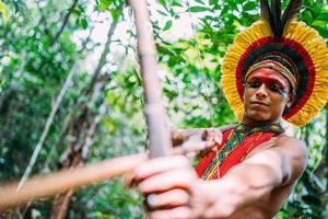 indiano della tribù pataxo usando arco e frecce. indiano brasiliano con copricapo di piume e collana foto