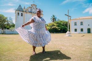 felice donna brasiliana di origine africana vestita con un tradizionale abito bahiano che balla davanti alla chiesa foto