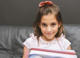 bambina che scrive nel quaderno. bella studentessa elementare che studia nel divano. foto