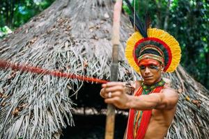 indiano della tribù pataxo usando arco e frecce. indiano brasiliano con copricapo di piume e collana foto
