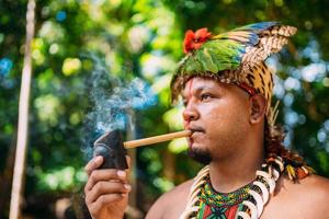 capo indiano della tribù pataxo che fuma la pipa . indiano brasiliano con copricapo di piume e collana foto