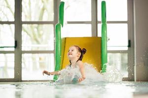 bambina che scivola giù dallo scivolo d'acqua foto