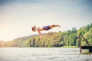 giovane uomo in forma che fa un salto in un lago. foto