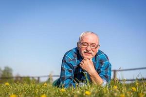 uomo anziano sdraiato sul campo estivo in erba verde. foto