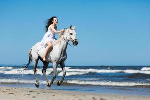 ragazza che attraversa la spiaggia su un cavallo bianco foto